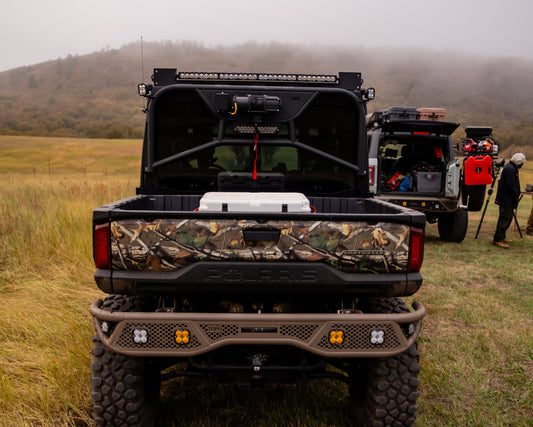 Camouflage Polaris Ranger with a TOPO headache rack in a field with mountains in the background